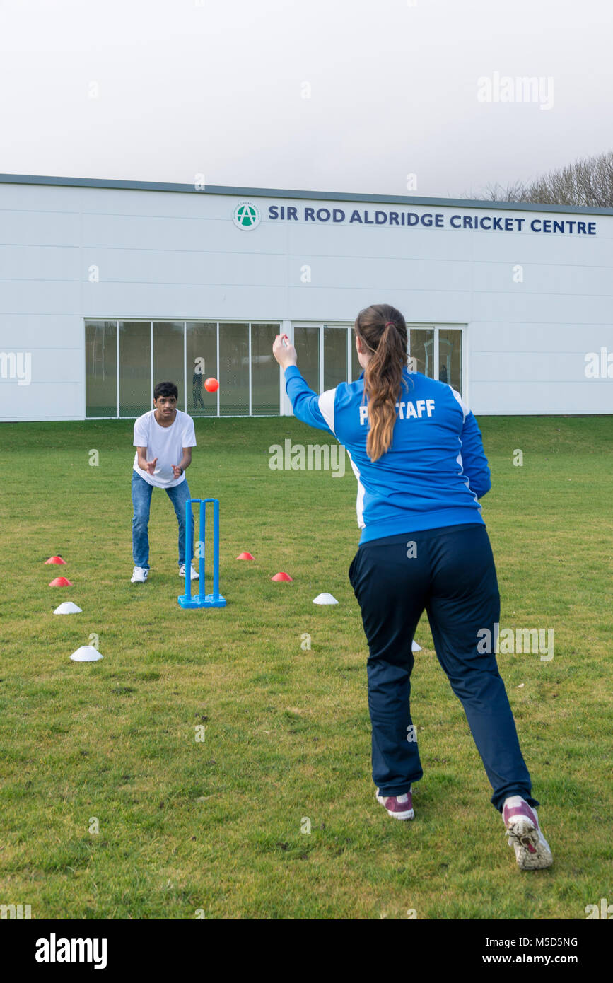 students practice playing cricket on a school playing field as part of a games lesson with their
