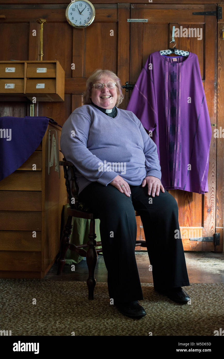 a female vicar sits in her office of a church in her vicars outfit