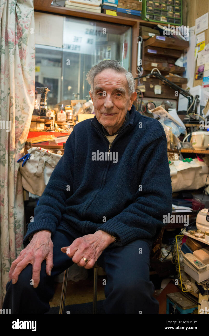 an old experienced watch repair man sits in his shop at his work bench Stock Photo