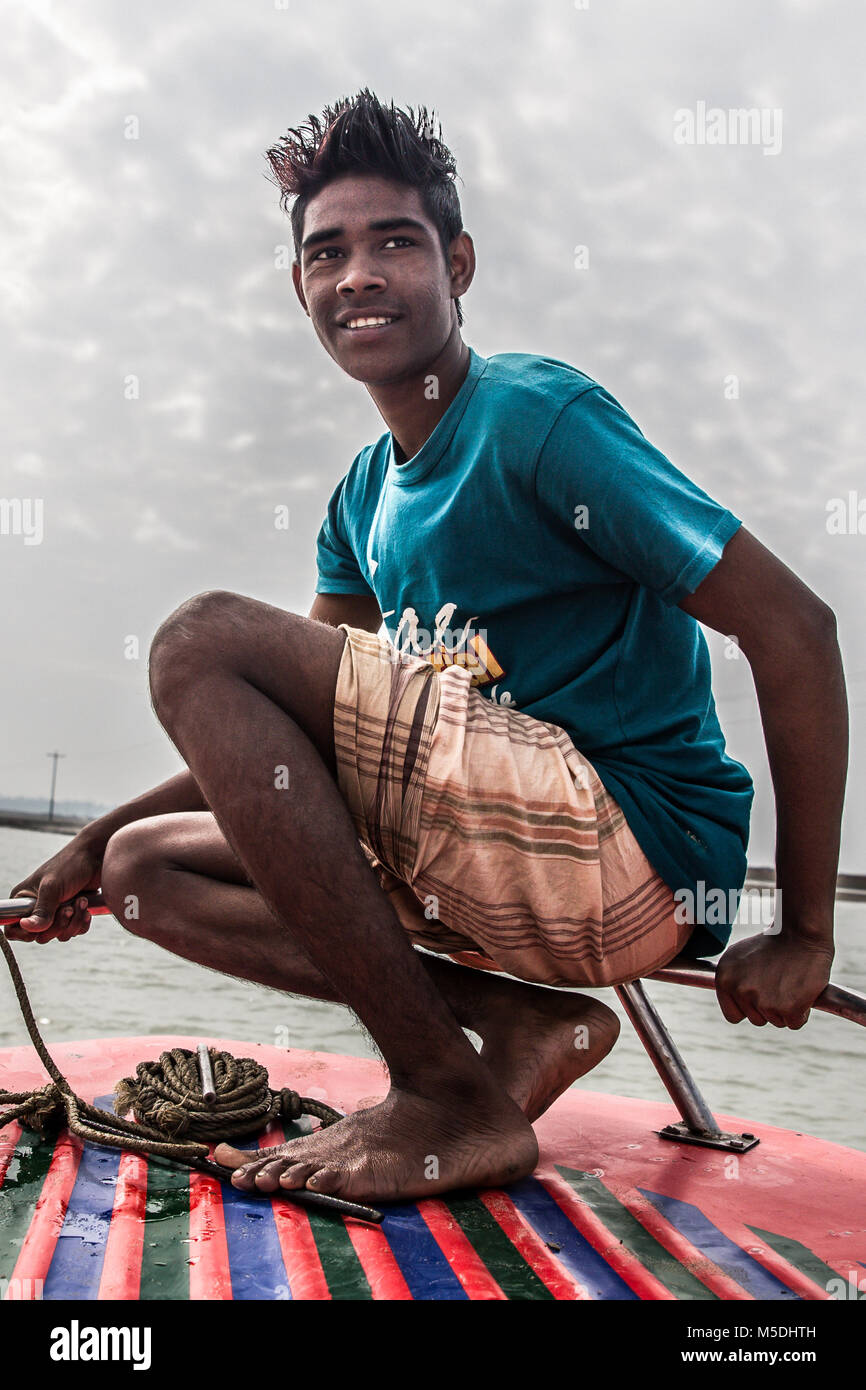 February 22, 2018 - Cox'S Bazar, Bangladesh - A young Bengali man poses for the camera on a boat near the Myanmar border. These men and their boats work tenuously connecting people from the Myanmar border to the Bangladesh mainland through the vast rivers that connect them. Unemployment rates in rural areas of Bangladesh are twice that of urban areas with people being thought of as being a burden to the whole family if they are not working. Here, I've concentrated on the positive side of a terrible situation showing the types of employment in and around the Cox's Bazar region of Bangladesh whe Stock Photo
