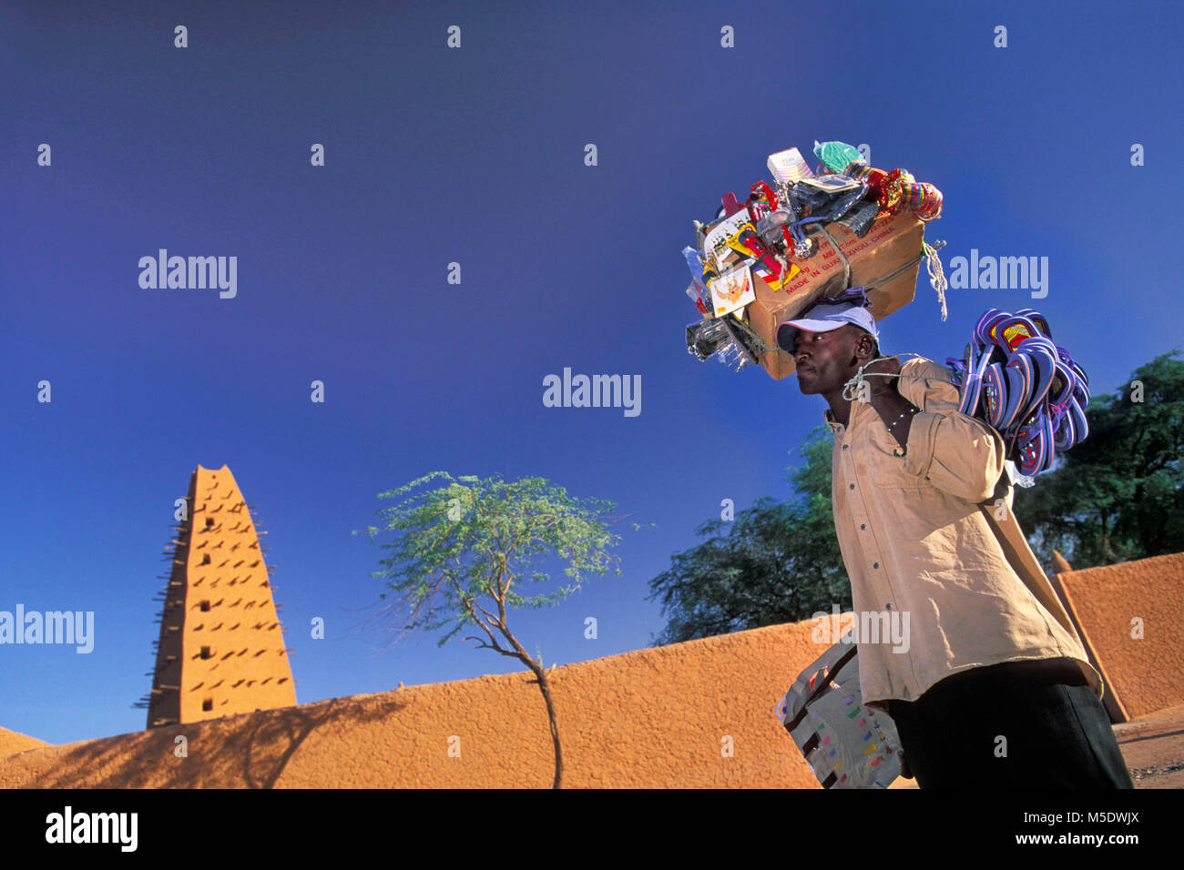 Niger. Agadez. Sahara desert. Sahel. Mosque. Man transporting his own grocery shop on his head. Unesco, World Heritage Site. Stock Photo