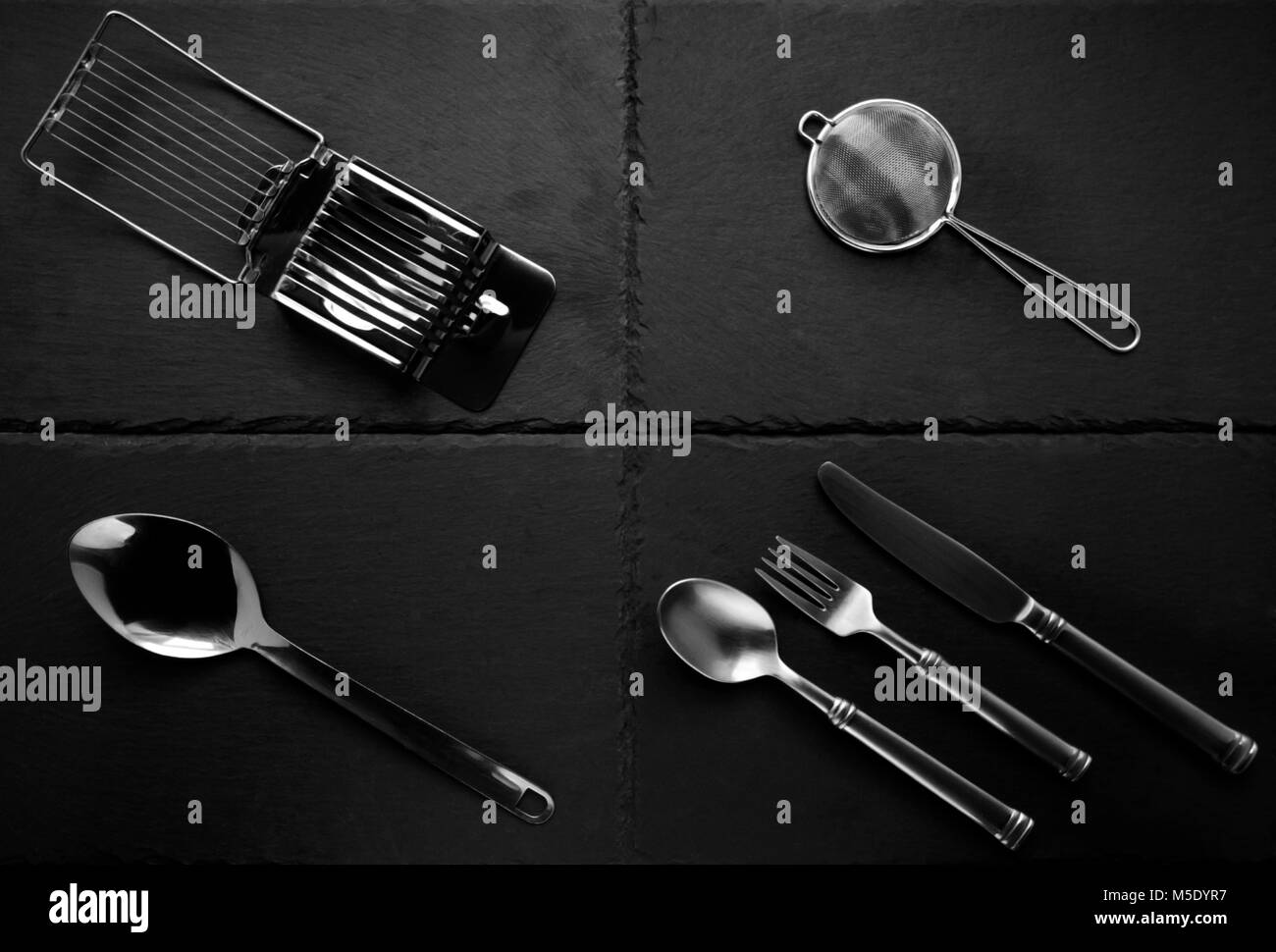 A selection of kitchen cutlery, and other items on slate tiles Stock Photo