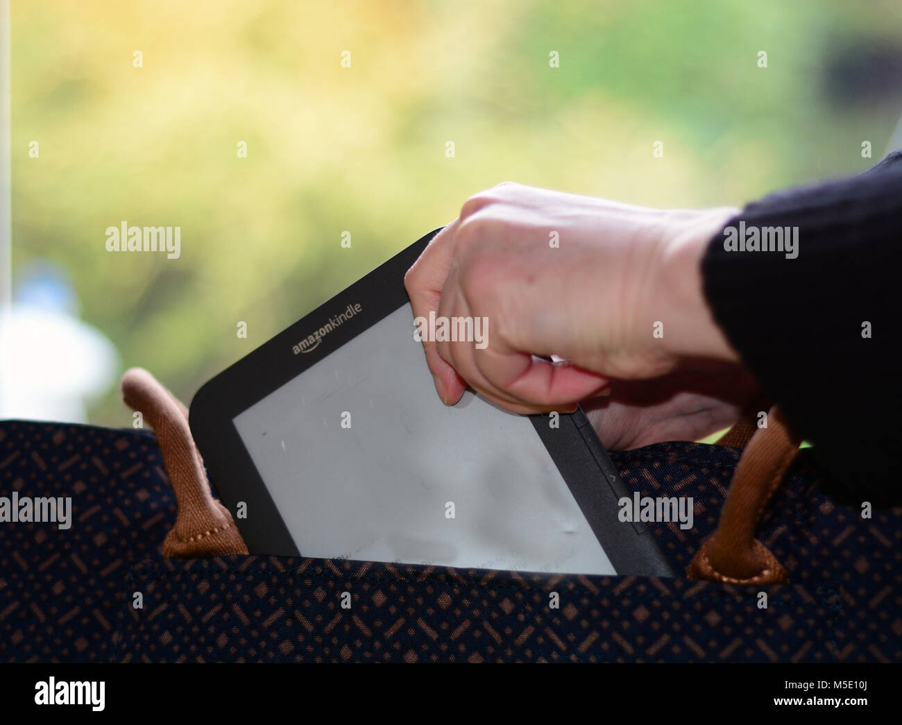 Woman putting a Kindle e-reader into her handbag (packing for holiday/morning commute concept) Stock Photo