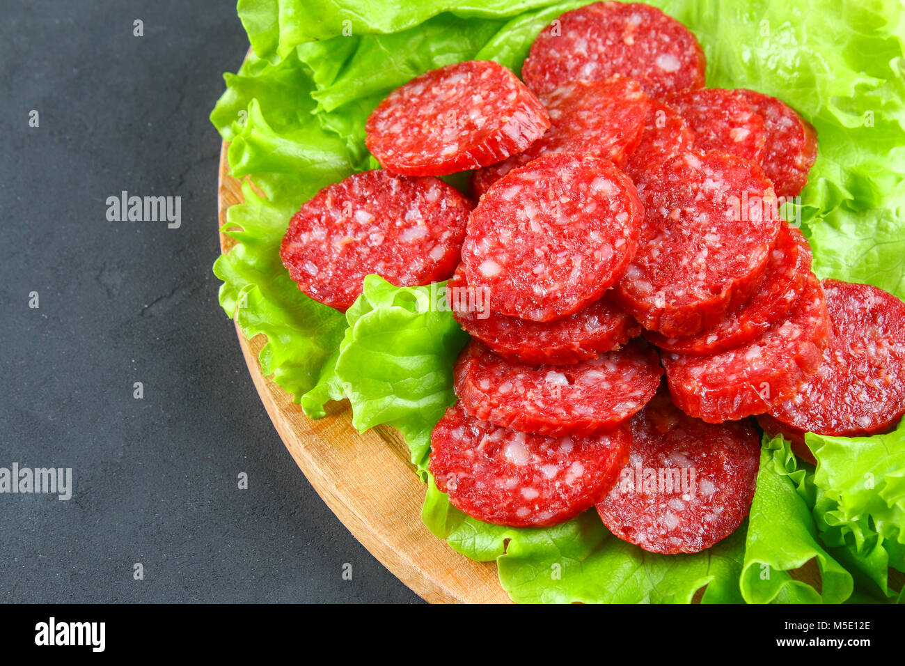 Smoked sausage, salami chopped in slices on a salad on a wooden circular cutting board on a concrete gray table Stock Photo