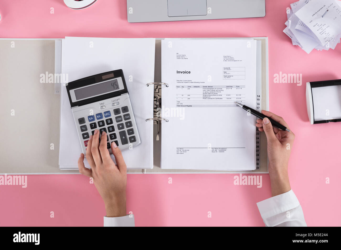 Close-up Of A Businesswoman Using Calculator While Calculating Invoice On Pink Desk Stock Photo