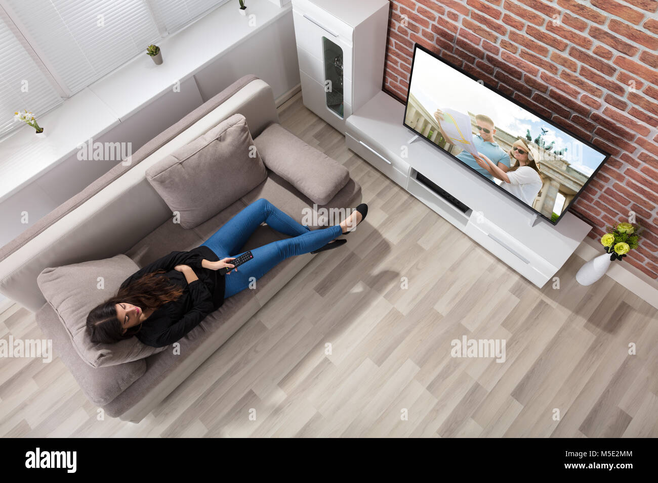 Elevated View Of A Woman Lying On Couch Watching Television At Home Stock Photo