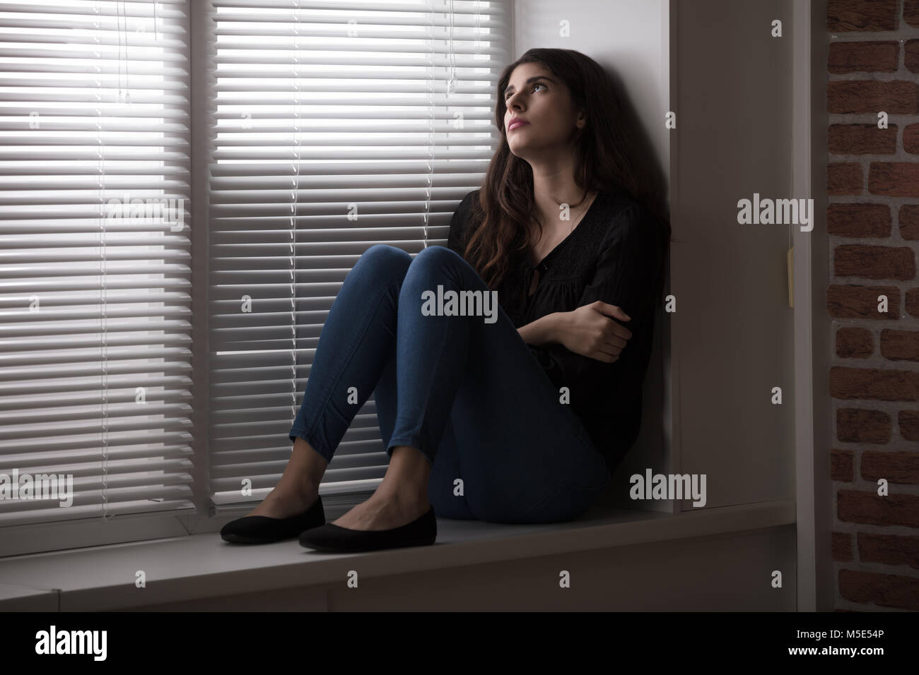 Pensive Young Woman Sitting On The Window Sill Stock Photo