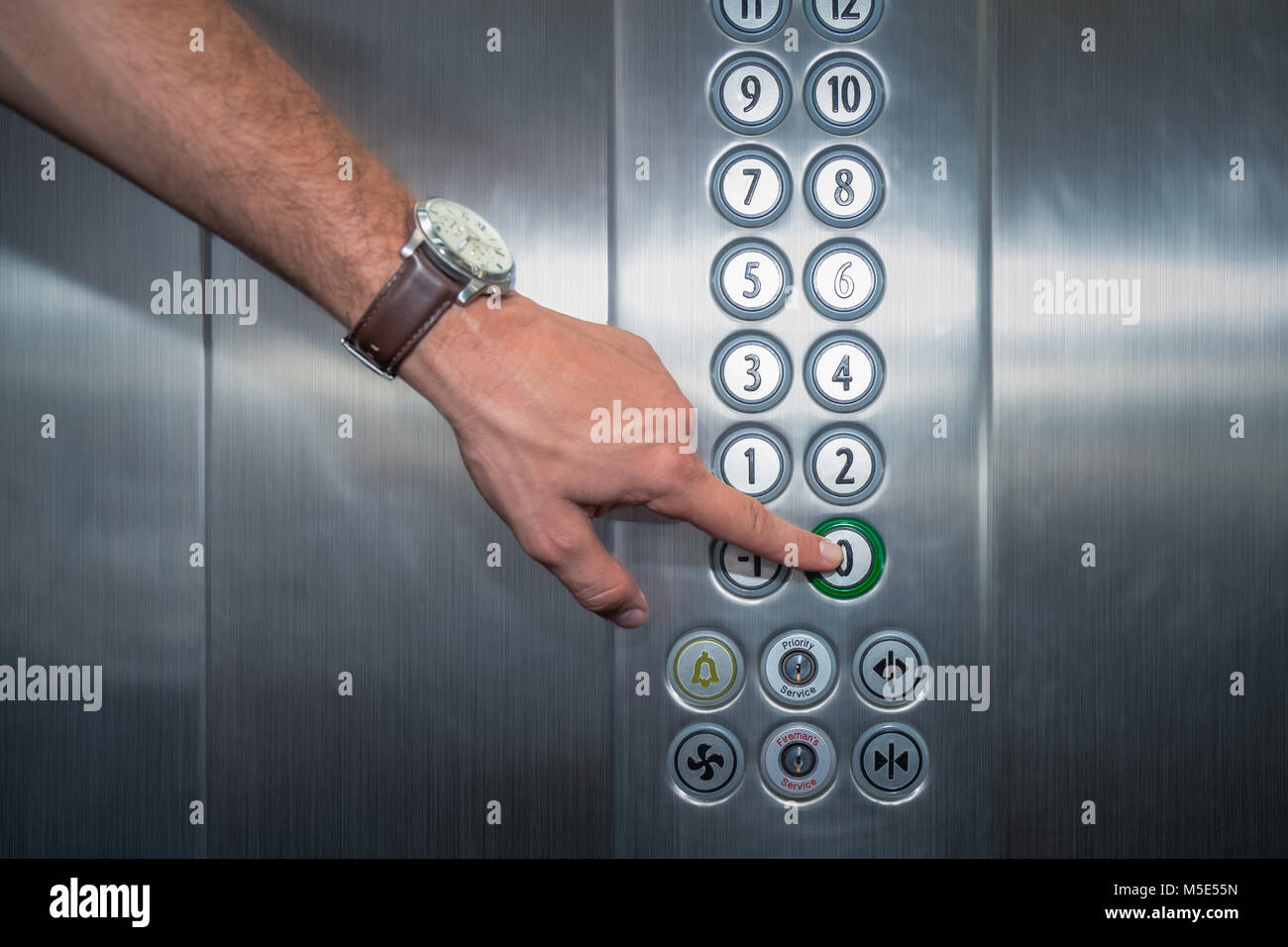 Male forefinger pressing the zero floor button in the elevator. Iron made interior. Stock Photo