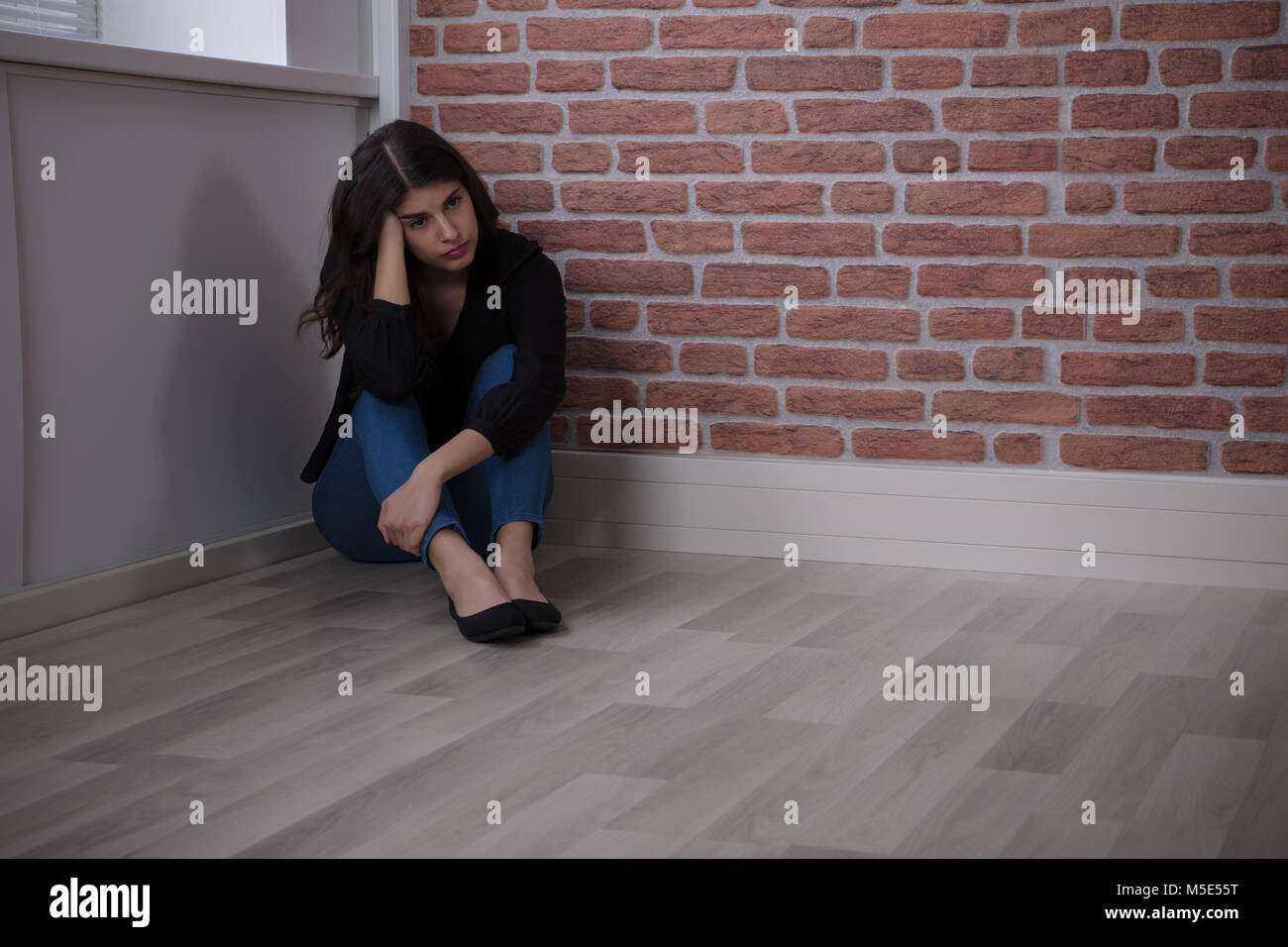 Sad Young Woman Sitting At The Corner Of The Room At Home Stock Photo
