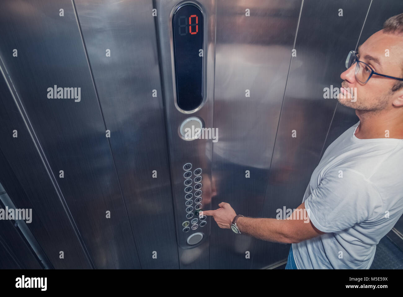 Young man in elevator pressing the zero floor button. Iron made interior. Stock Photo