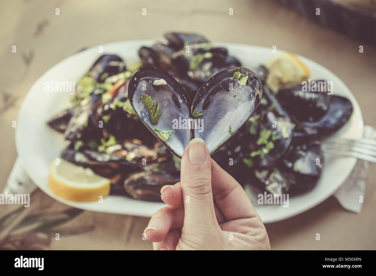 Close up of female hand holding opened heart shaped mussel at the restaurant table. Sea food and healthy eating concepts. Stock Photo