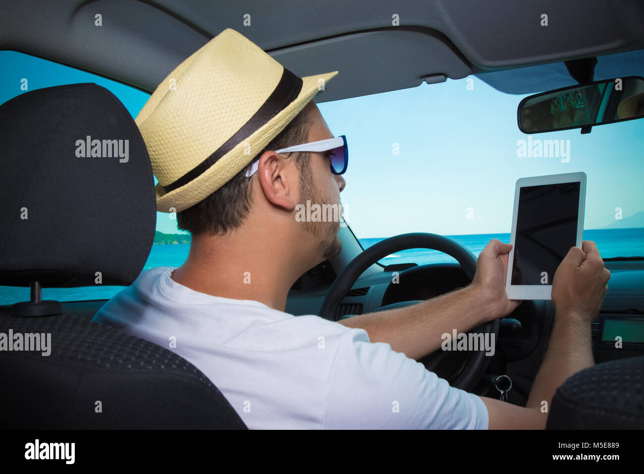 Happy tourist in car looking at tablet device. Sea in the background. Travel, vacation, and gps navigation concepts. Stock Photo