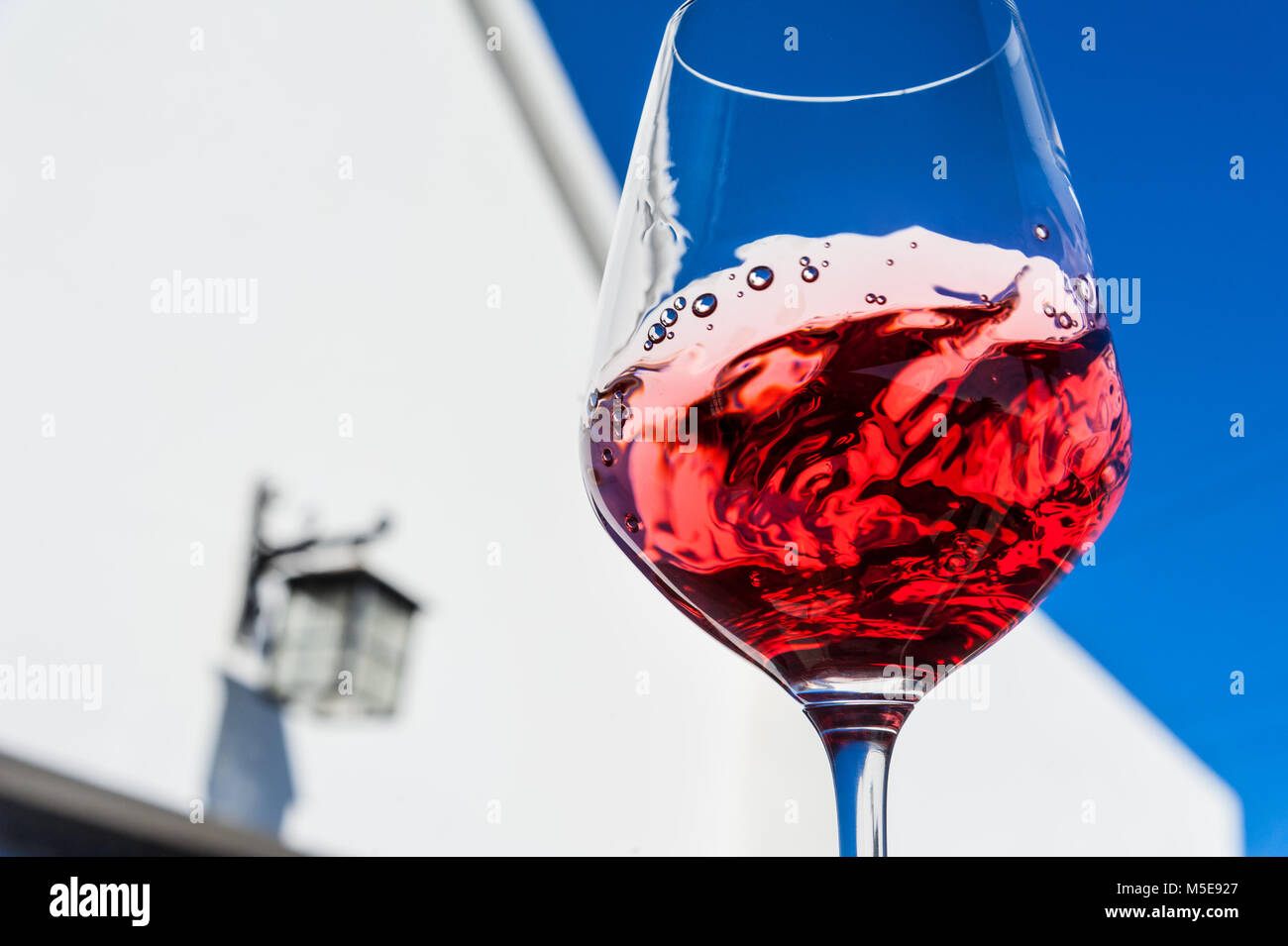 ALFRESCO RED WINE TASTING DRINKING Swirling and evaluating a glass of fine light red wine in outdoor alfresco sunny blue sky wine tasting situation Stock Photo