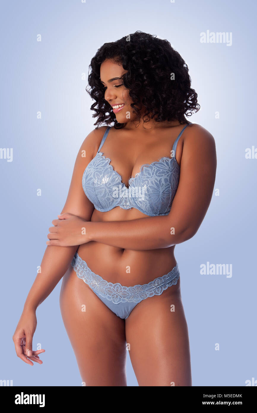 Beautiful happy plus size sexy woman with curly hair in light blue lingerie bra and thong underwear. Stock Photo
