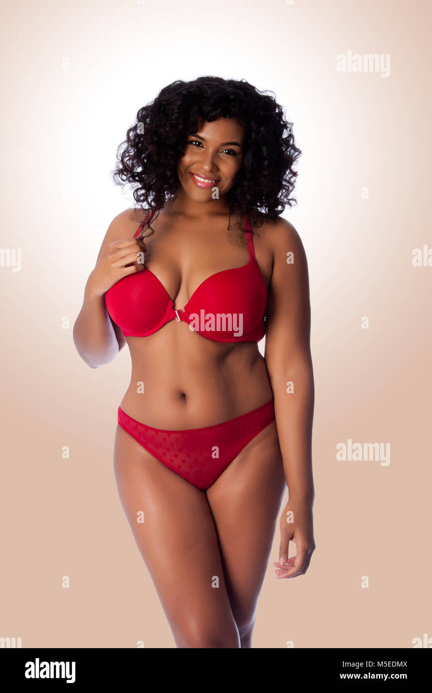 Beautiful happy plus size sexy woman with curly hair in red lingerie bra and thong underwear. Stock Photo