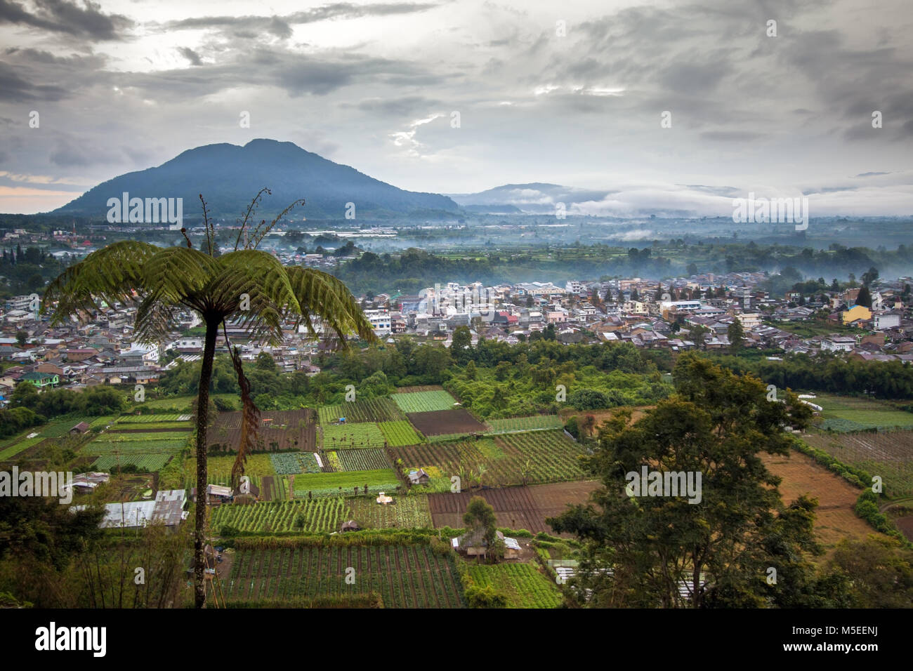 Stormy weather surrounds mountains of Berastagi a rural Sumatran Town. High angle view with contrasting rural and urban town with wide angle landscape Stock Photo