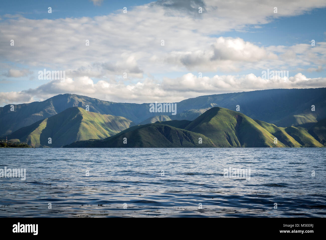 Majestic landscape and scenery from far lake shore of the volcanic crater Lake Toba. Green mountains seen from water surface low angle view of nature Stock Photo
