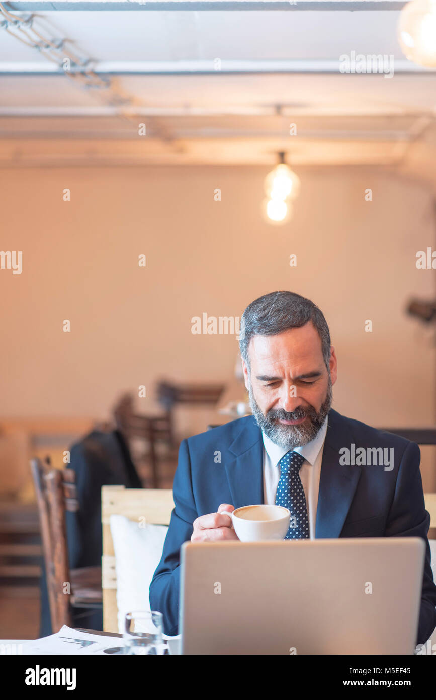 Senior mature business man having a coffee in a coffee shop and working on his computer Stock Photo