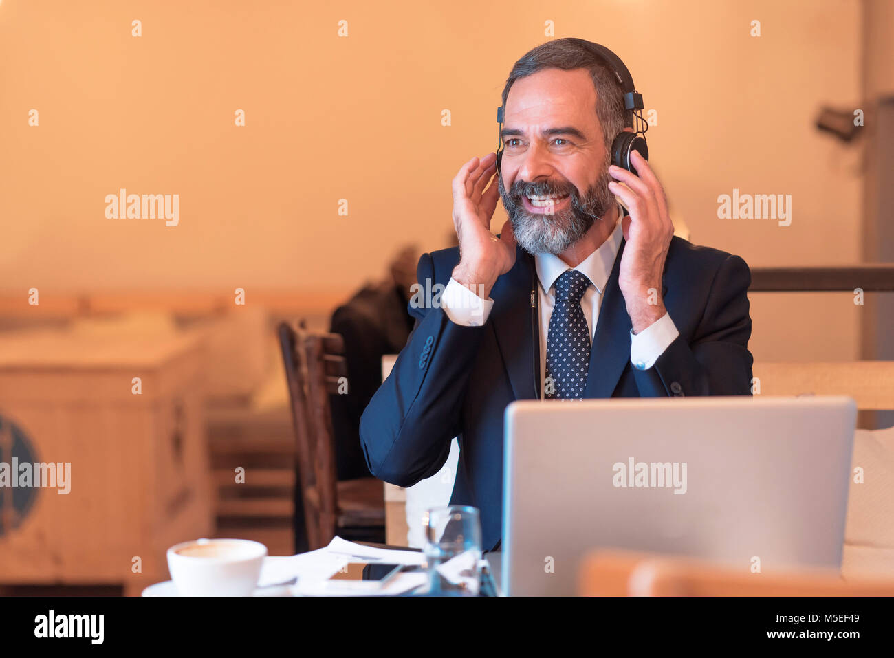 Senior old business man listening to his favorite music through a pair of big headphones in a coffee shop Stock Photo