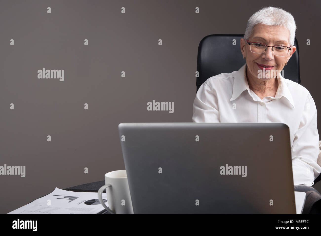 Satisfied senior business woman reading some news on her laptop in office Stock Photo