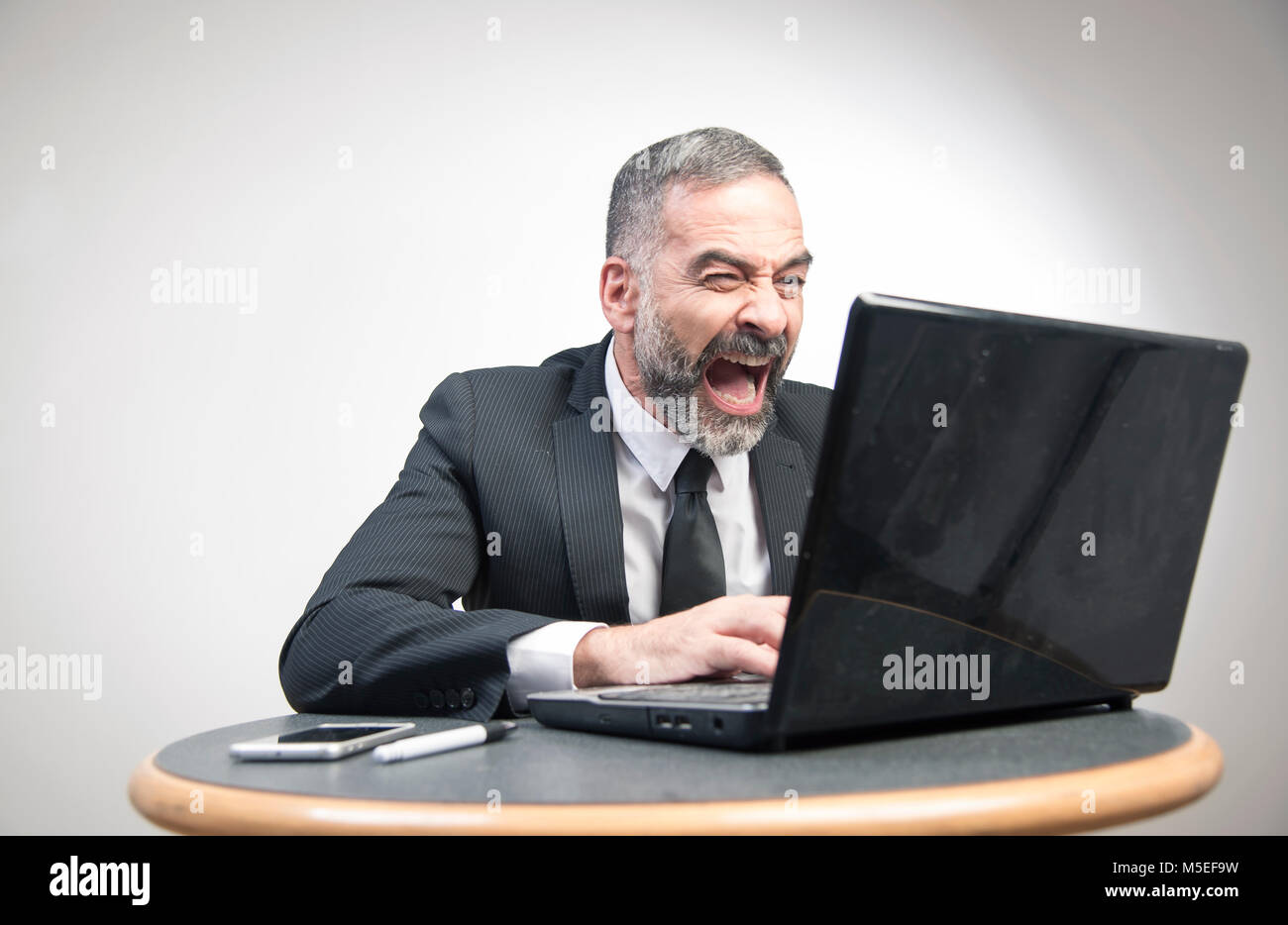 Senior business man shouting at his laptop, furious and frustrated with an email he receives Stock Photo