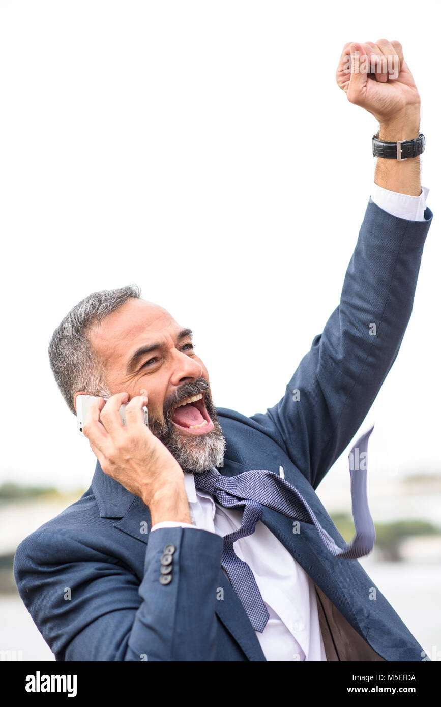 Cheering victorious senior business man receiving great news over his cell phone Stock Photo