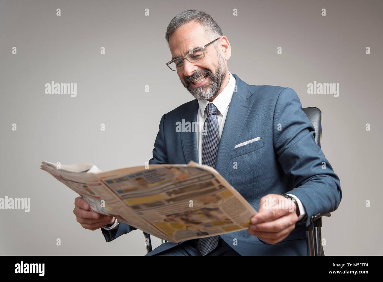 Happy senior business man reading newspaper, amused with its content Stock Photo