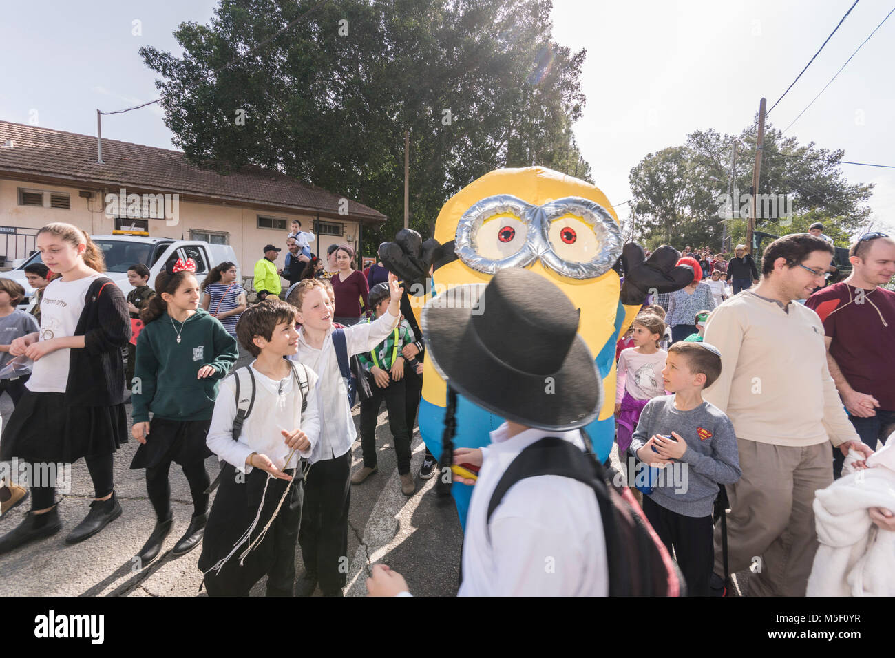Elkana, Israel. 23rd February, 2018. Kids and parents walk near a Minion customed man, in a parade celebrating the upcoming Jewish holiday of Purim. On this holiday, marking an ancient tradition about Jews being saved from destruction, many people and virtually all kids wear Costumes. Credit: Yagil Henkin/Alamy Live News Stock Photo
