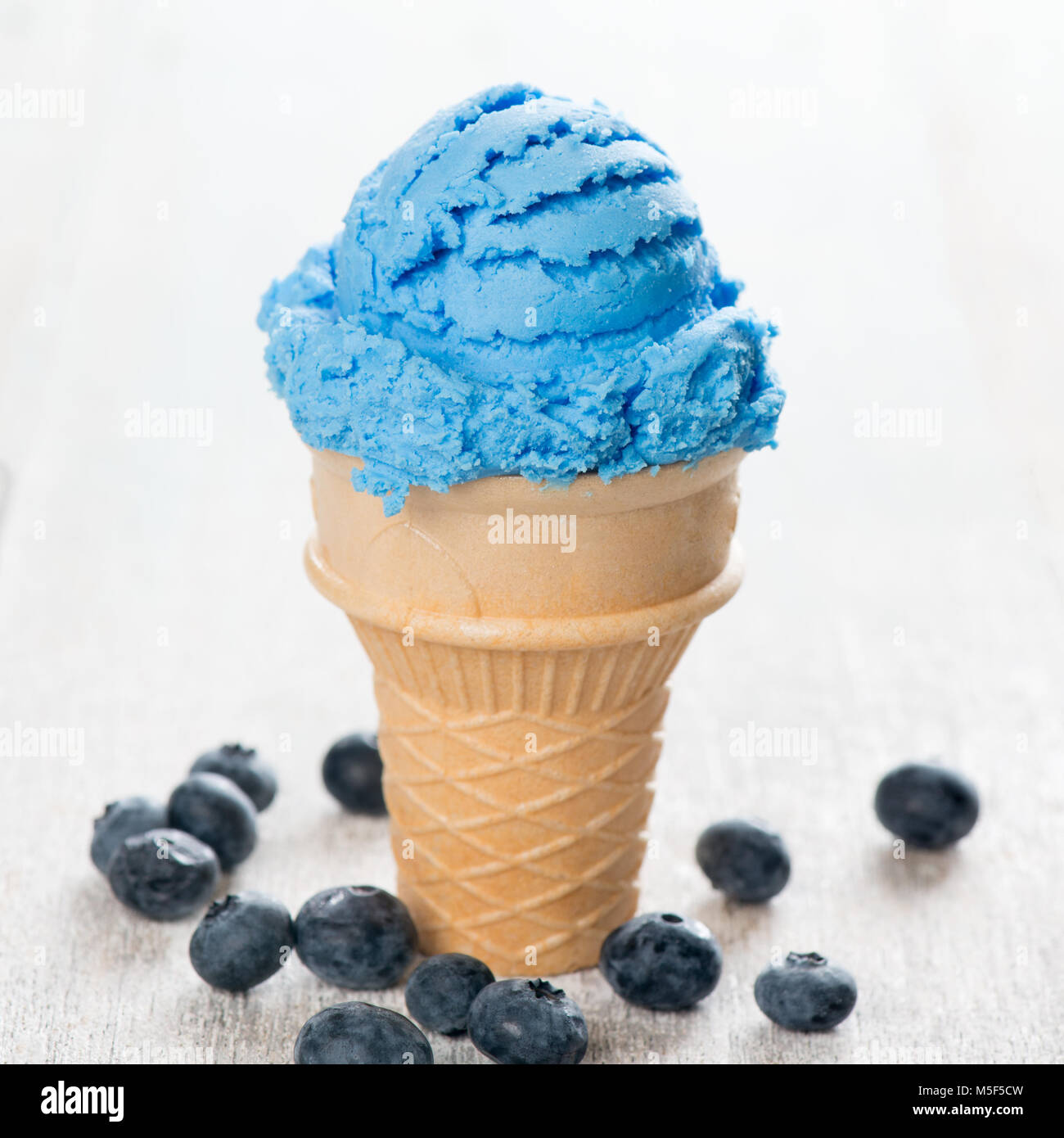 Blue ice cream in waffle cone with blueberry fruit on white wooden ...