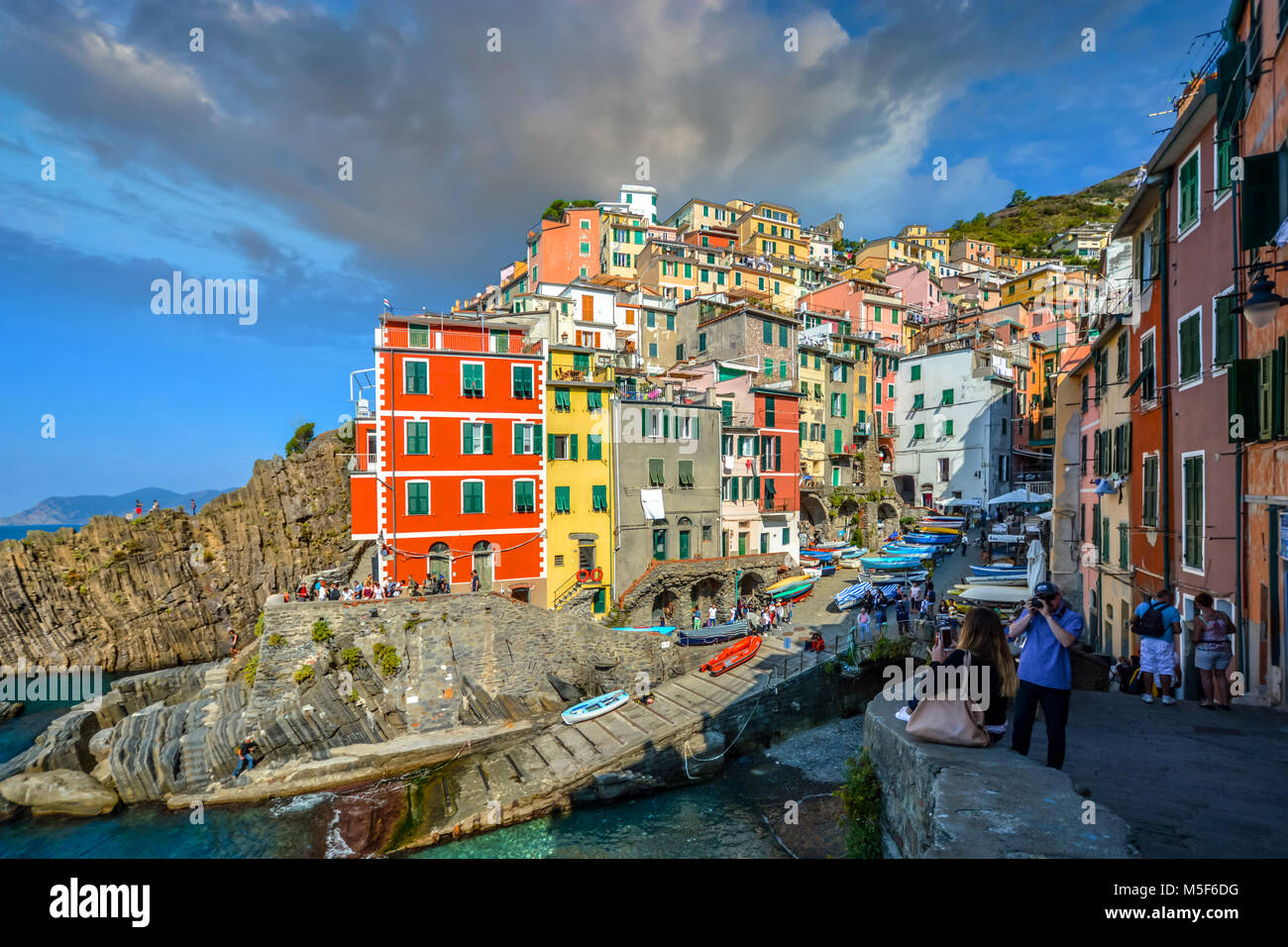 Tourists enjoying a summer morning at the colorful fishing village and harbour at Riomaggiore Italy, part of the Cinque Terre on the Italian Riviera Stock Photo