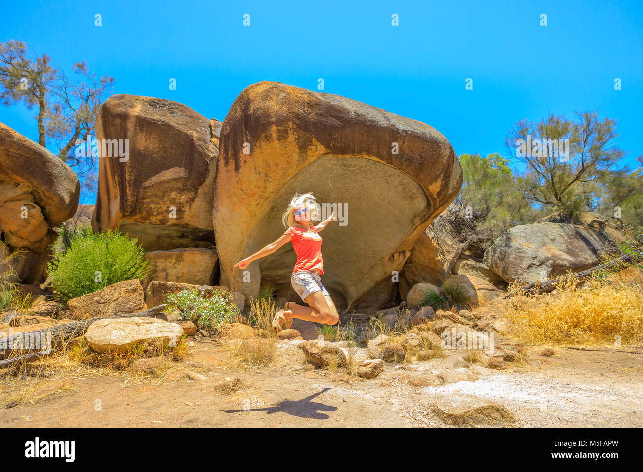 Australian outback freedom concept. Happy Caucasian woman jumping at Hippo's Yawn, a hippo-shaped rock near Wave Rock in Hyden, Western Australia. Female jumper in Hyden Wildlife Park. Stock Photo