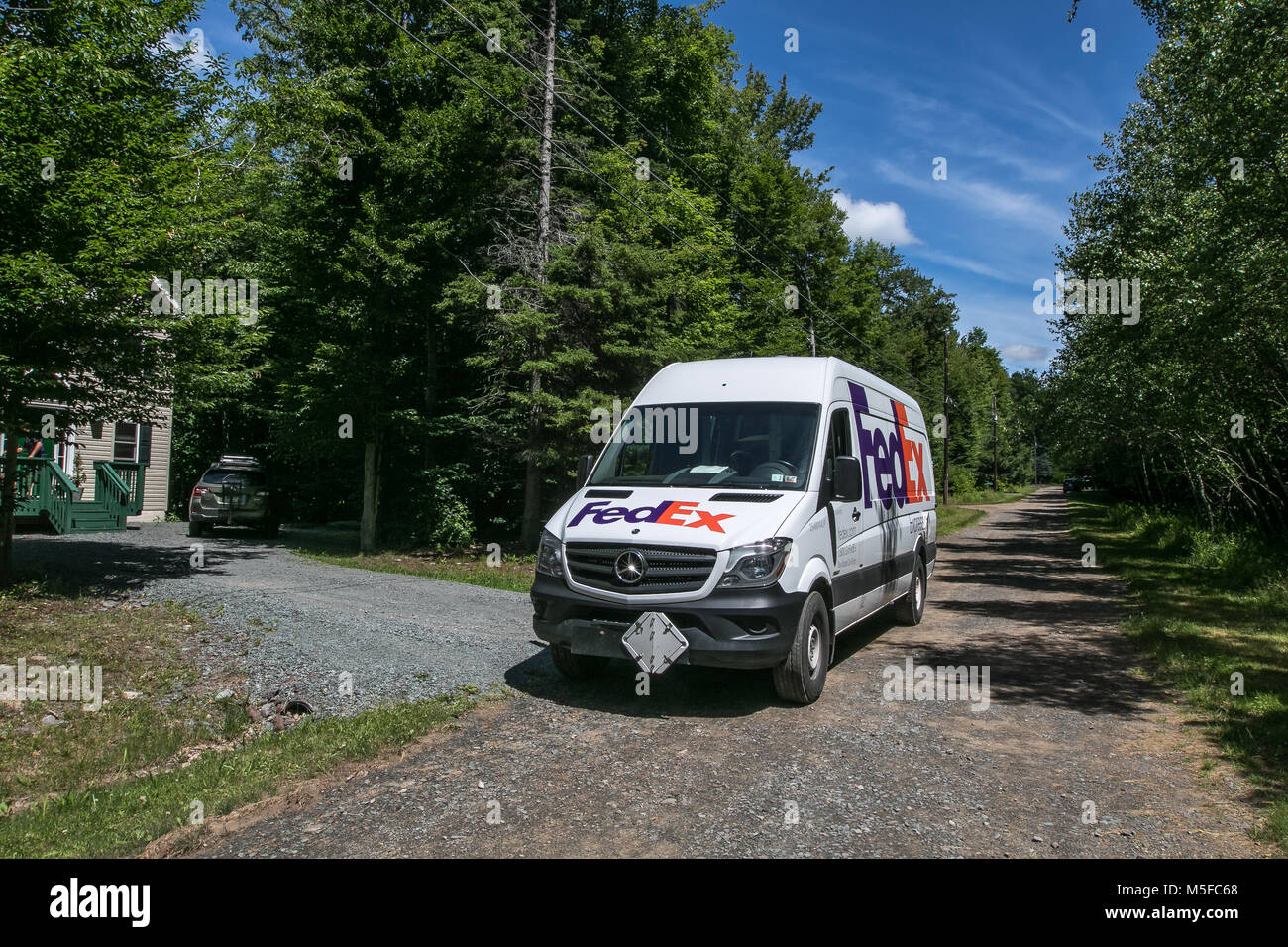 FedEx van is parked by a house where the employee is making a delivery. Stock Photo
