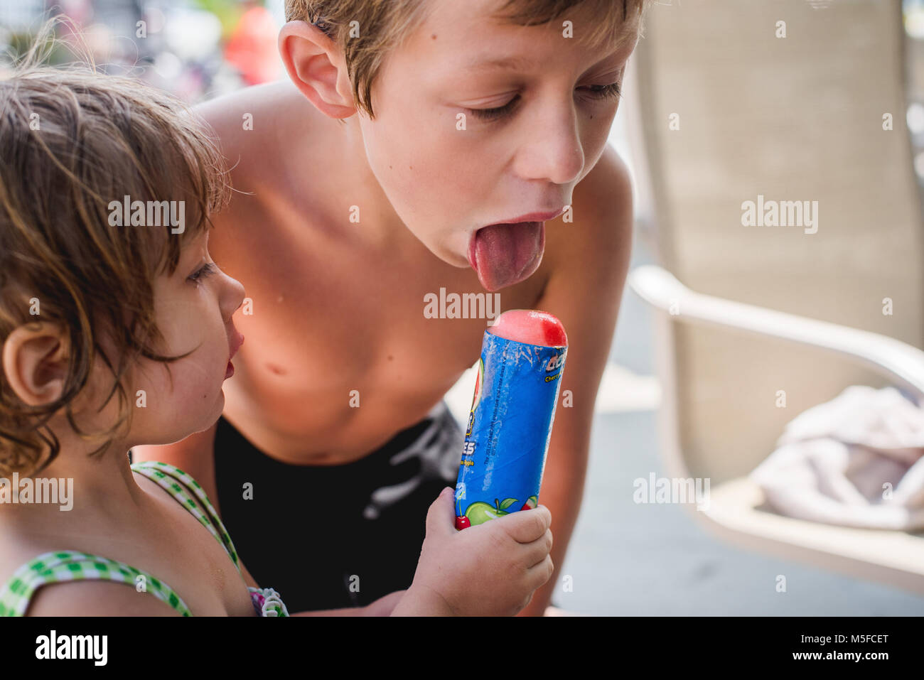 A young boy takes a lick from a push up ice cream being held by a toddler girl during the summer. Stock Photo