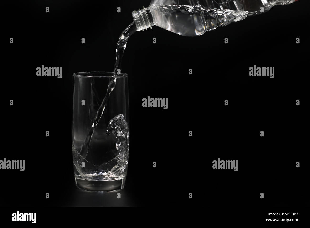 water is poured from plastic bottle into glass isolated on black Stock Photo