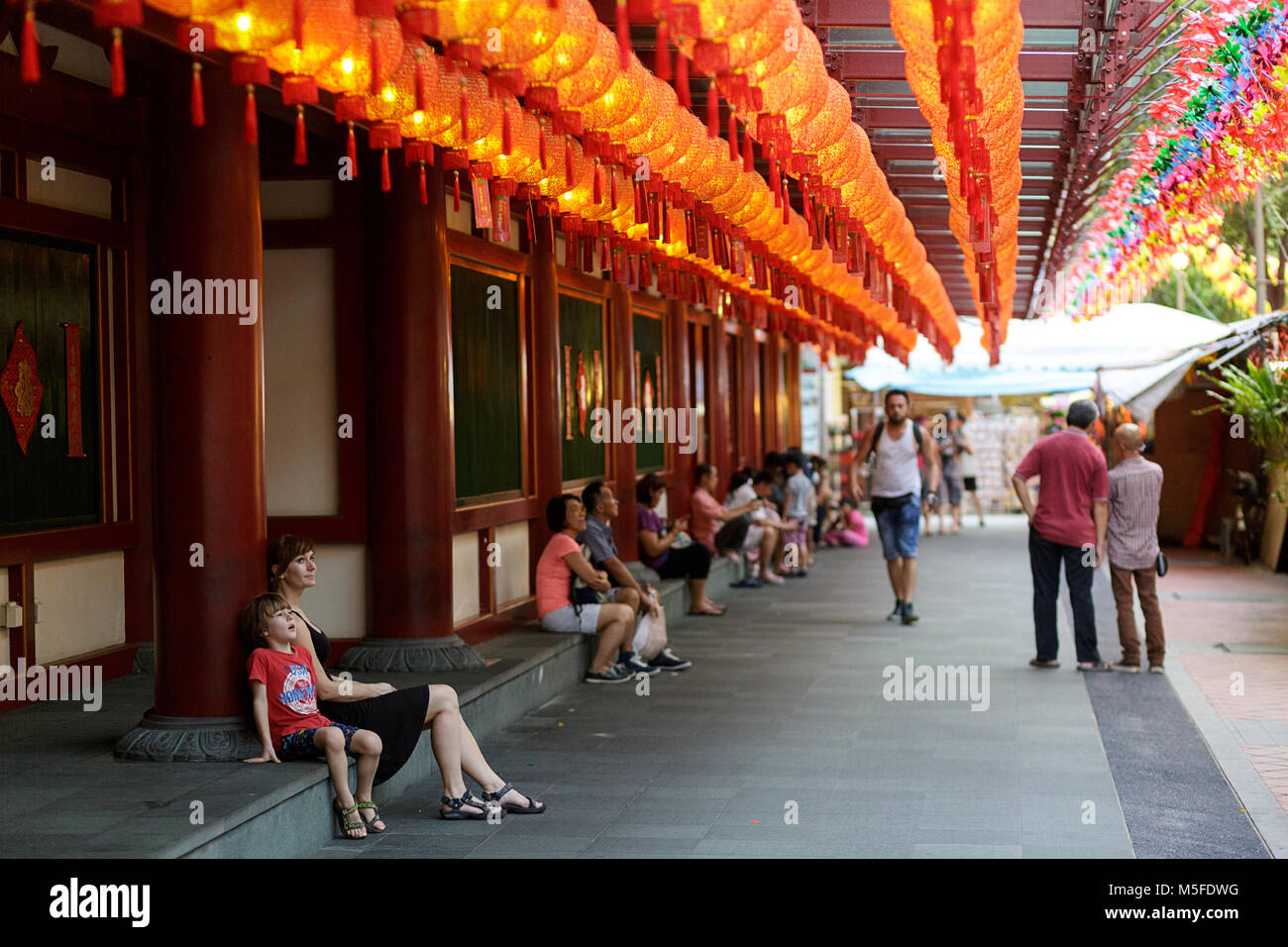 Woman in black dress and cute western boy sitting by the walkway at Buddha Tooth Relic Temple under red lanterns for the chinese new year, Singapore Stock Photo