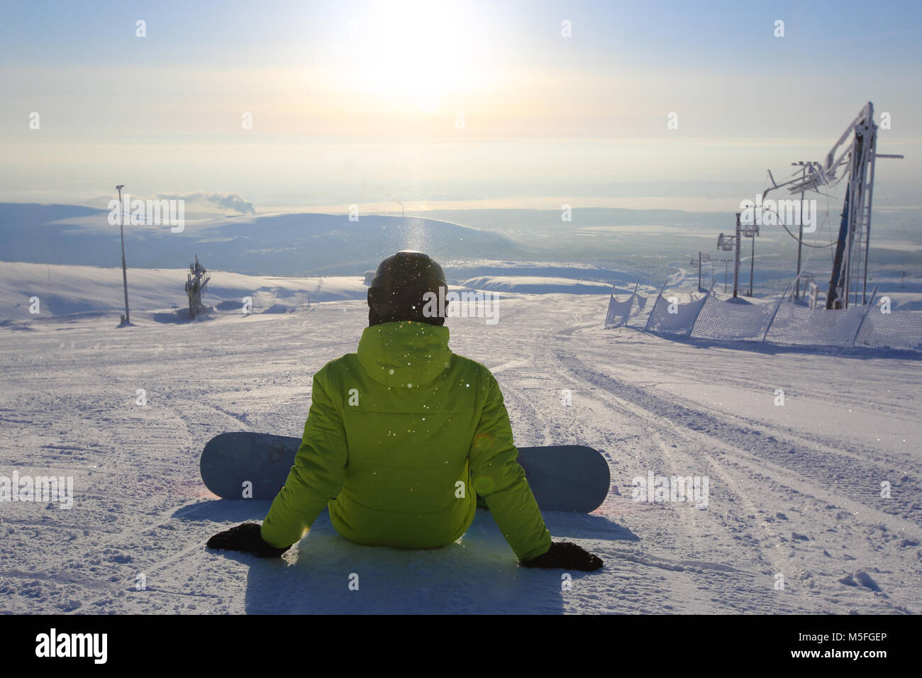 Snowboarder sitting on snow slope of ski resort, rear view Stock Photo