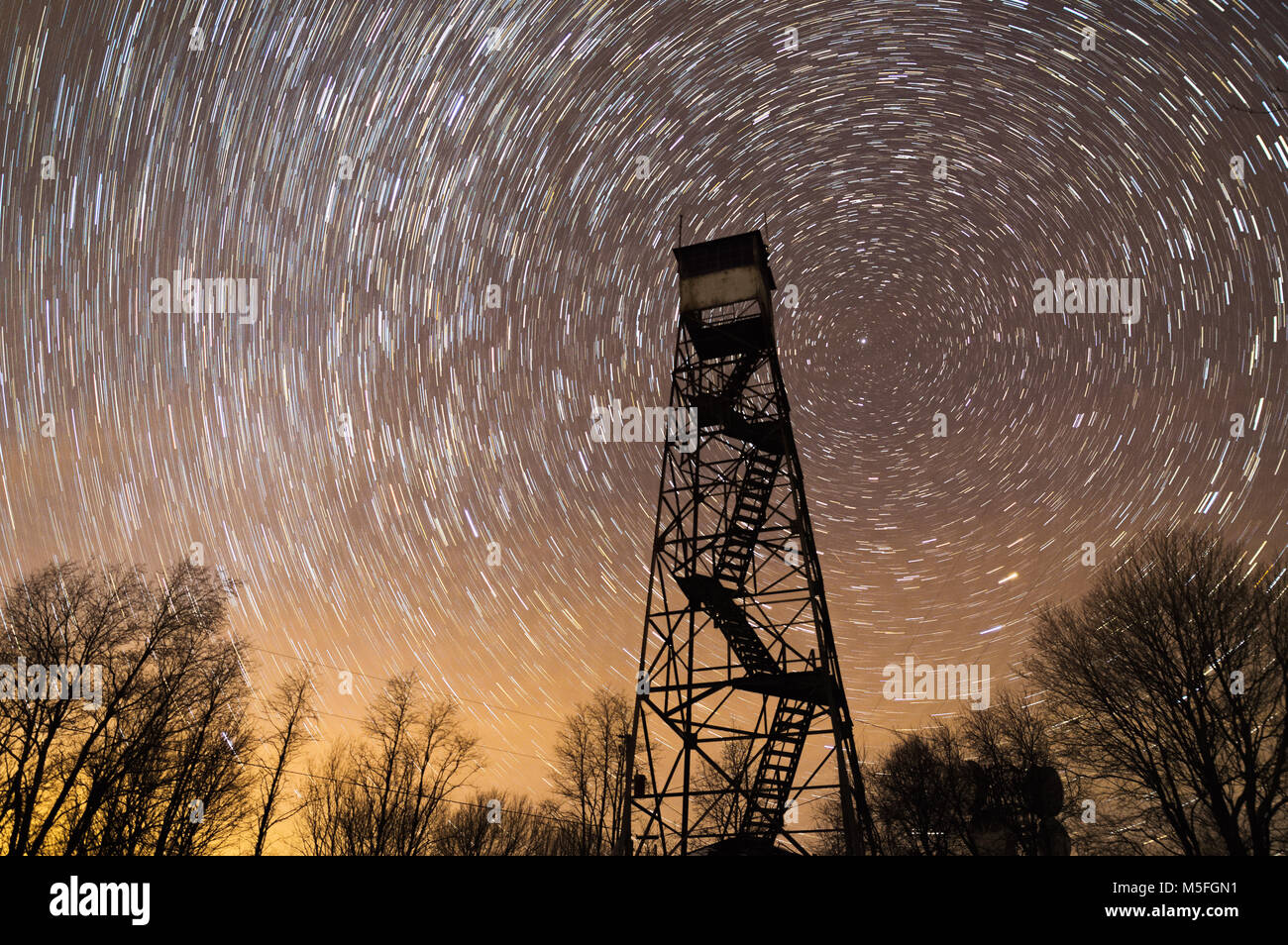 An abandoned fire tower stands silhouetted against the dark night sky as stars circle around the north star. Stock Photo