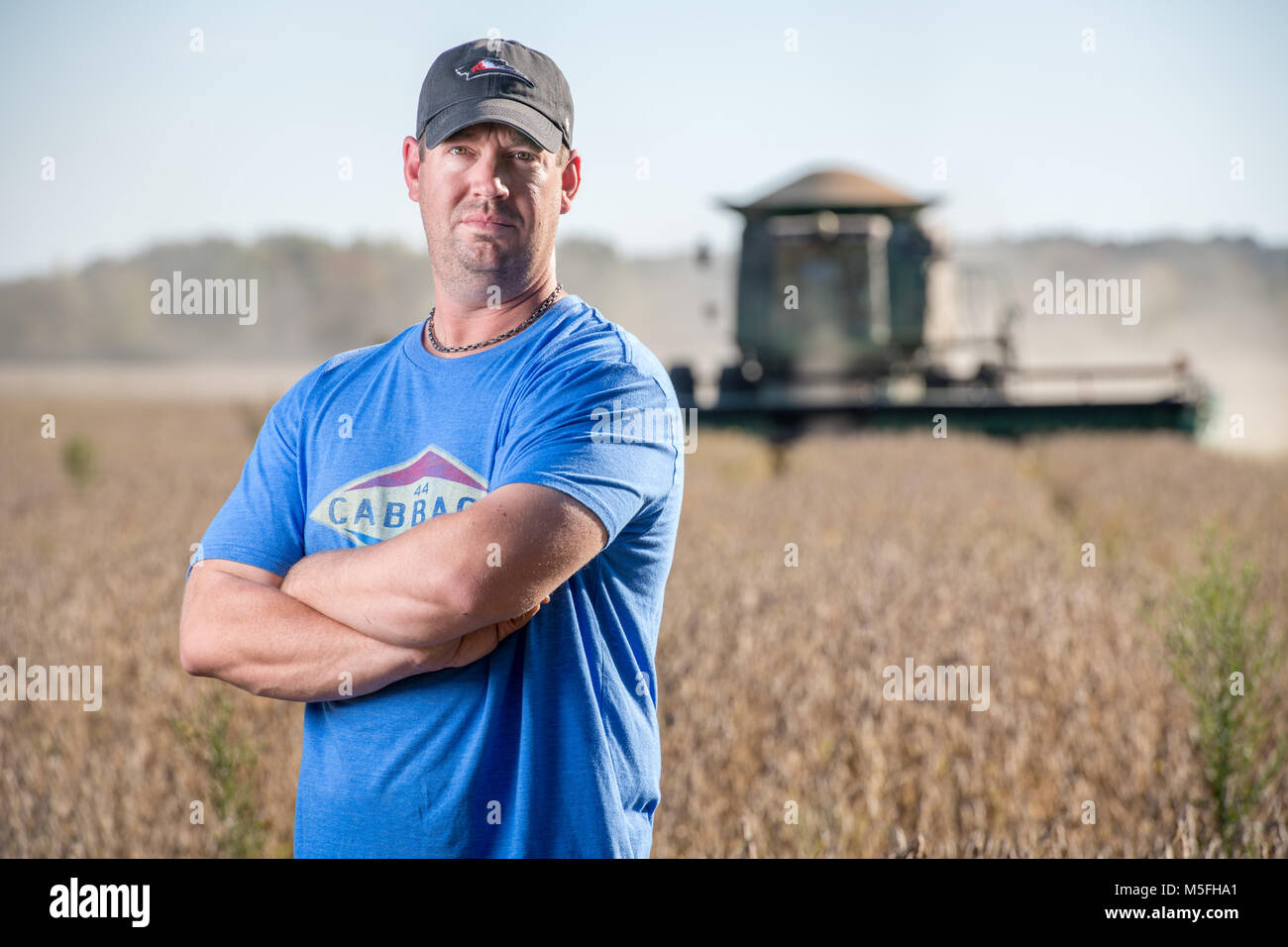 Confident male farmer stands with his arms crossed in soybean field ...