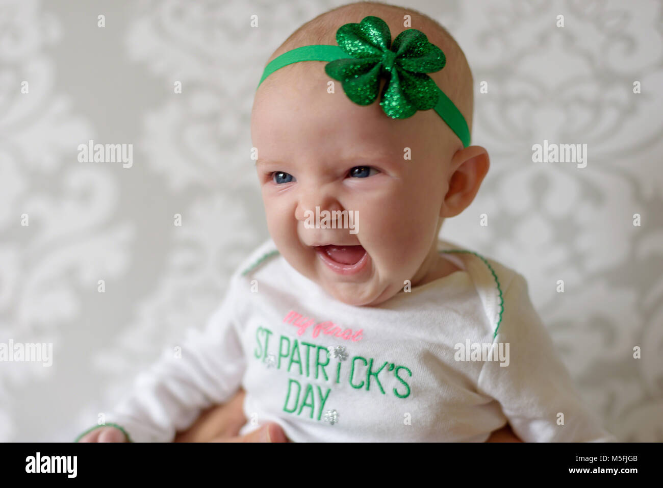 Irish baby with big blue eyes laughing and wearing St Patricks Day outfit and shamrock headband Stock Photo