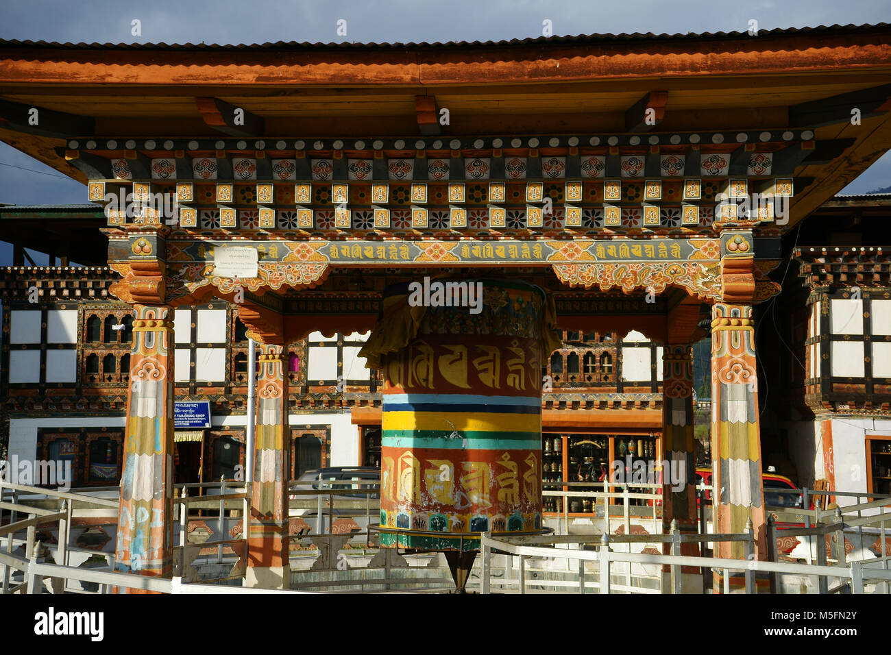 Buddhist prayer wheel in central town square of Paro with souvenir stores behind, Paro valley, Bhutan Stock Photo