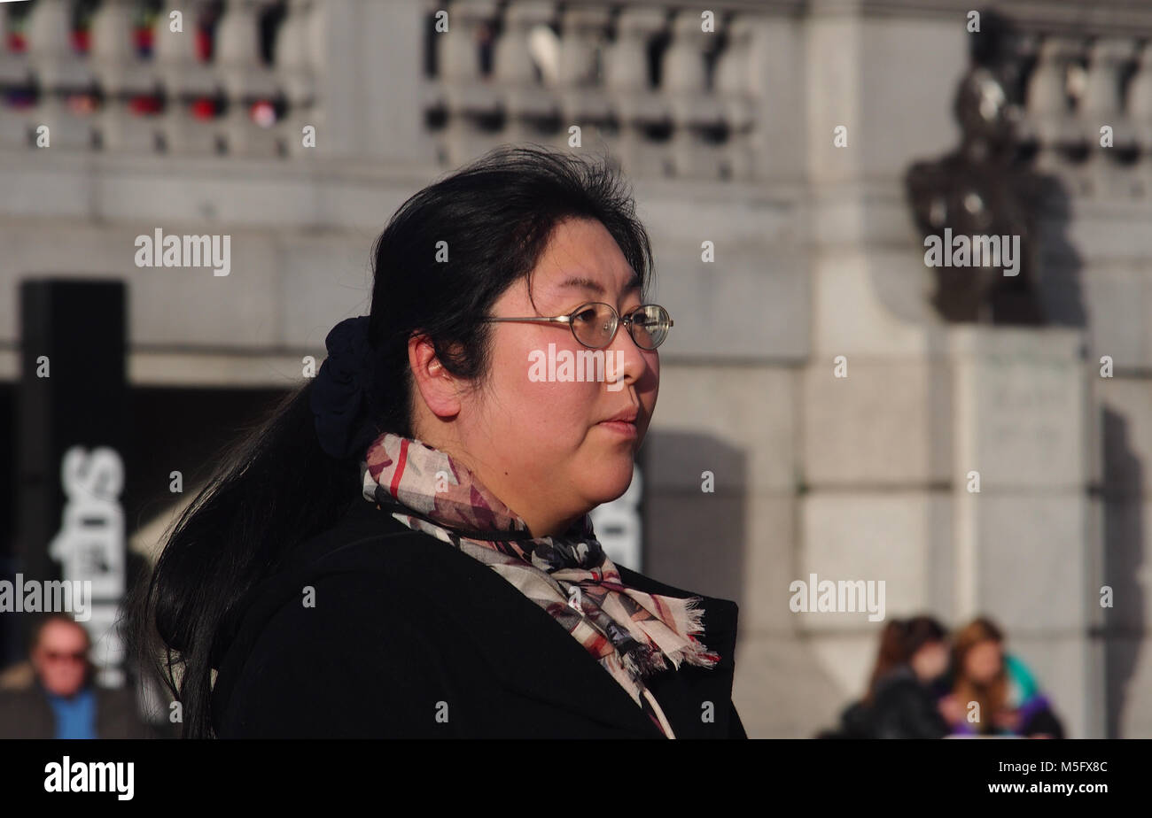 Head and shoulders of an oriental woman standing in Trafalgar Square, London wrapped up in a scarf and coat in winter sunshine Stock Photo