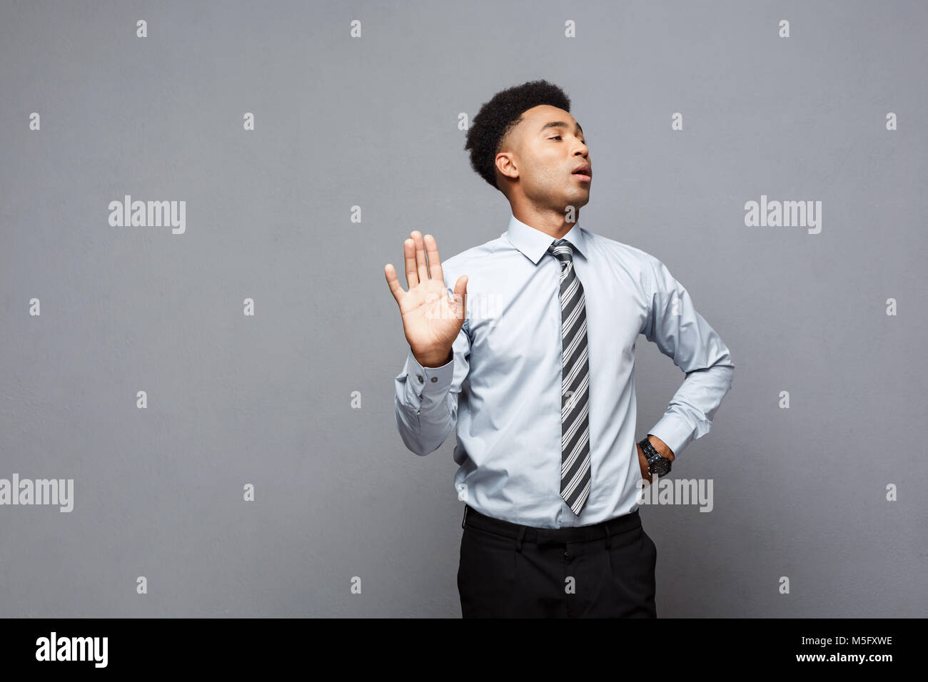 Business concept - portrait of stressed African American business man showing stop sign with hand on grey background. Stock Photo