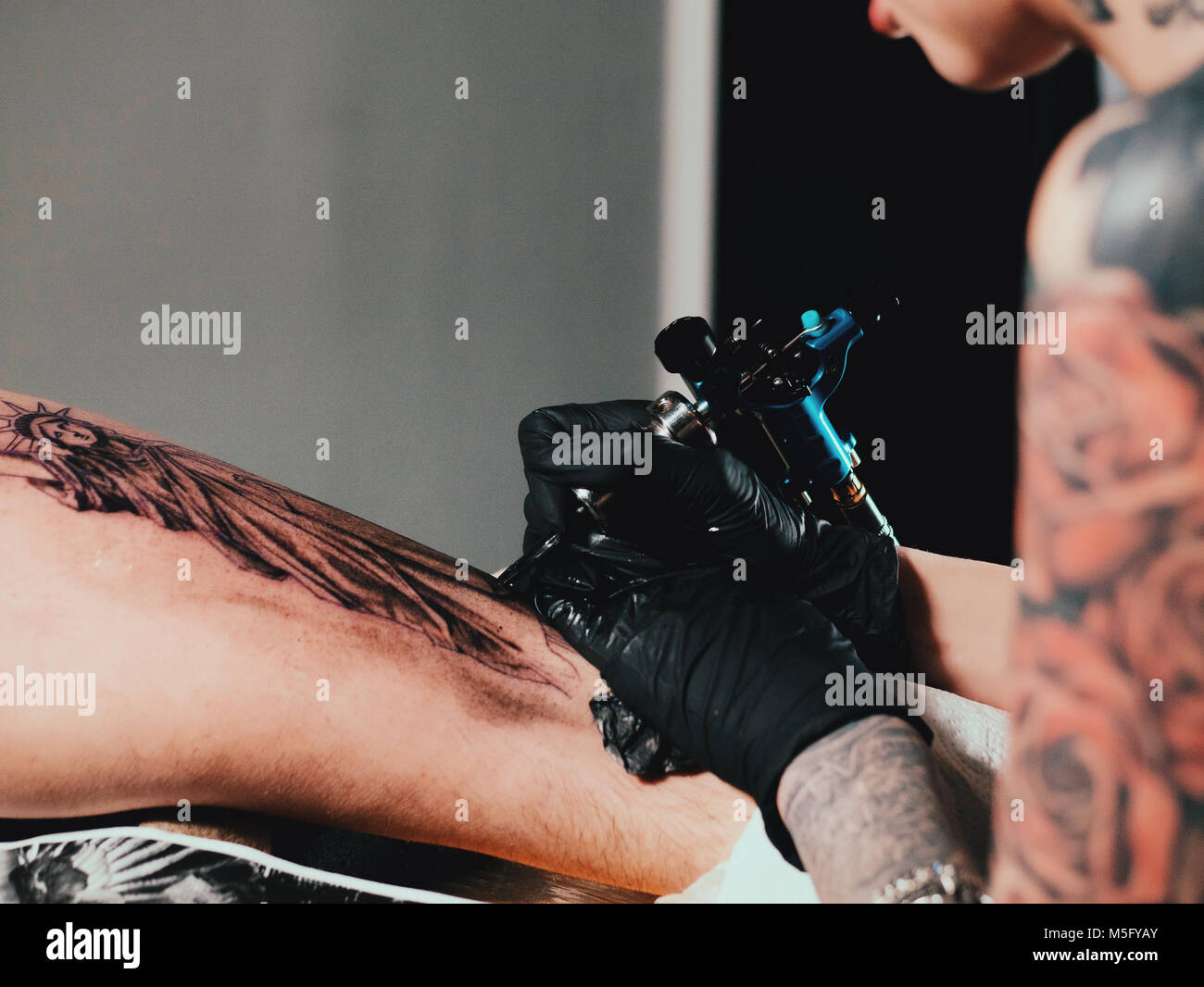 The tattoo artist at work. Woman in black latex glove tattooing statue