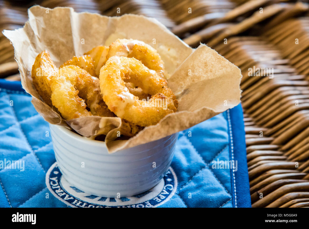 Fried calamari rings and chips, top view macro photo, food photography. Fish and chips in paper, white dish, blue background, closeup, low angle view. Stock Photo