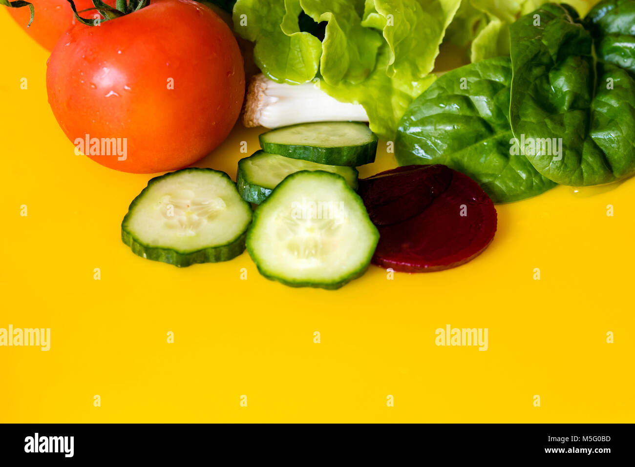 Fresh colourful salad ingredients, yellow background, room for text. Lettuce, spring onion, tomato, beetroot and cucumber slices, closeup. Stock Photo