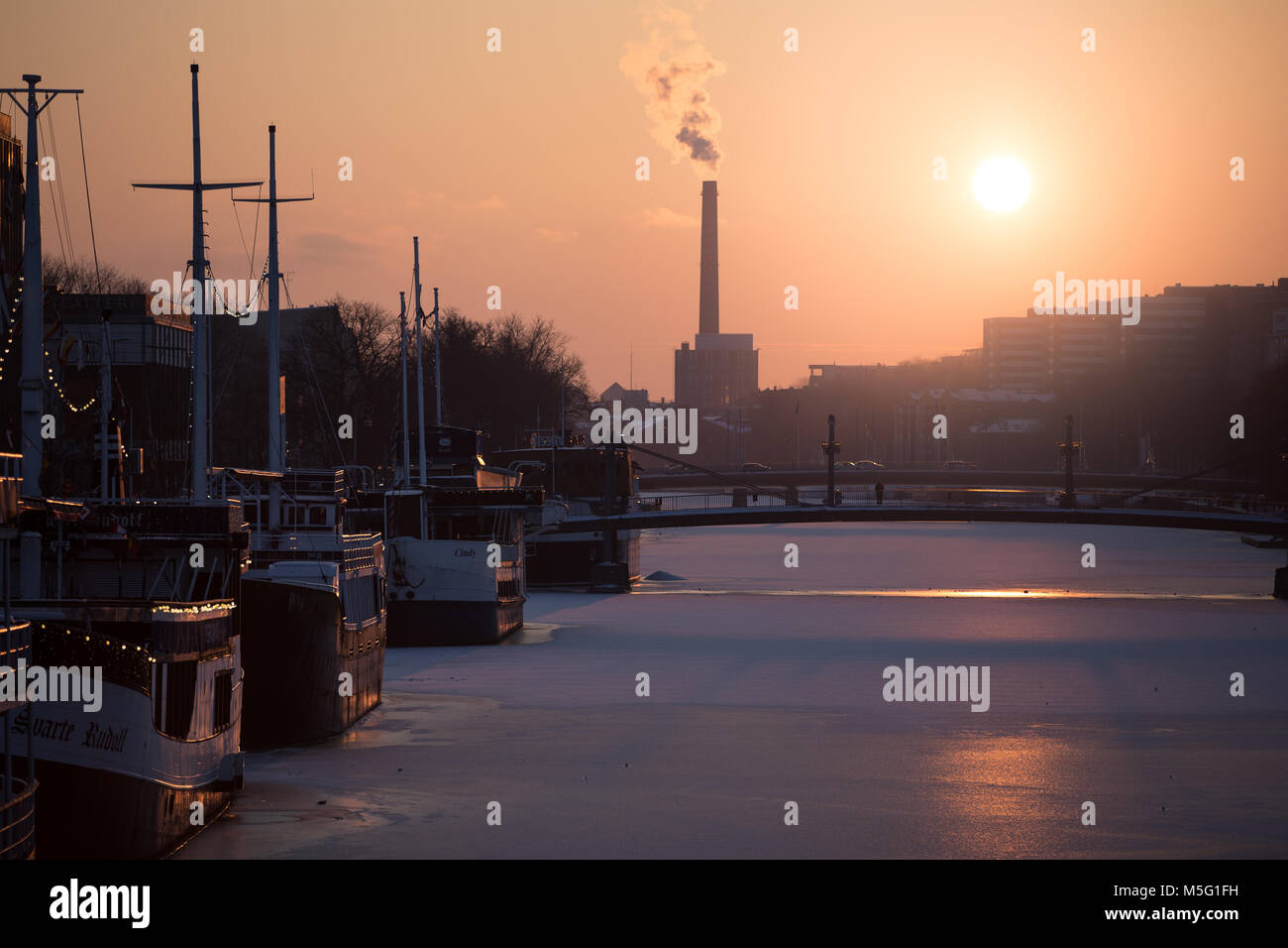 TURKU, FINLAND - FEBRUARY 18th, 2018: Golden sunset at winter  over Aura river with the popular river boat restaurants on the frozen river and Turku E Stock Photo