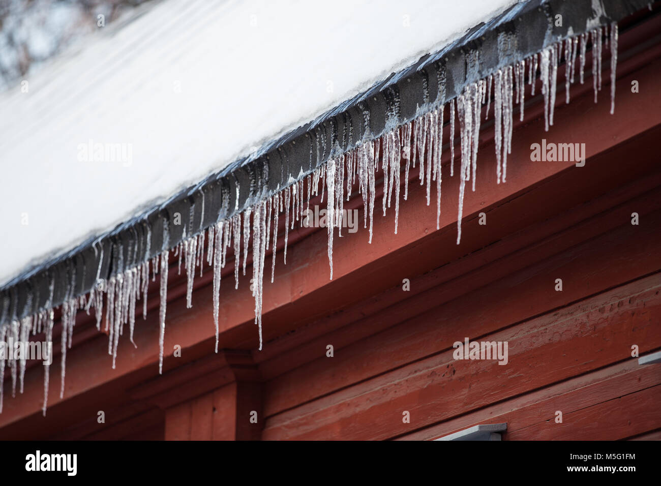 Detail of icicles hanging from snow covered roof on red wooden building Stock Photo