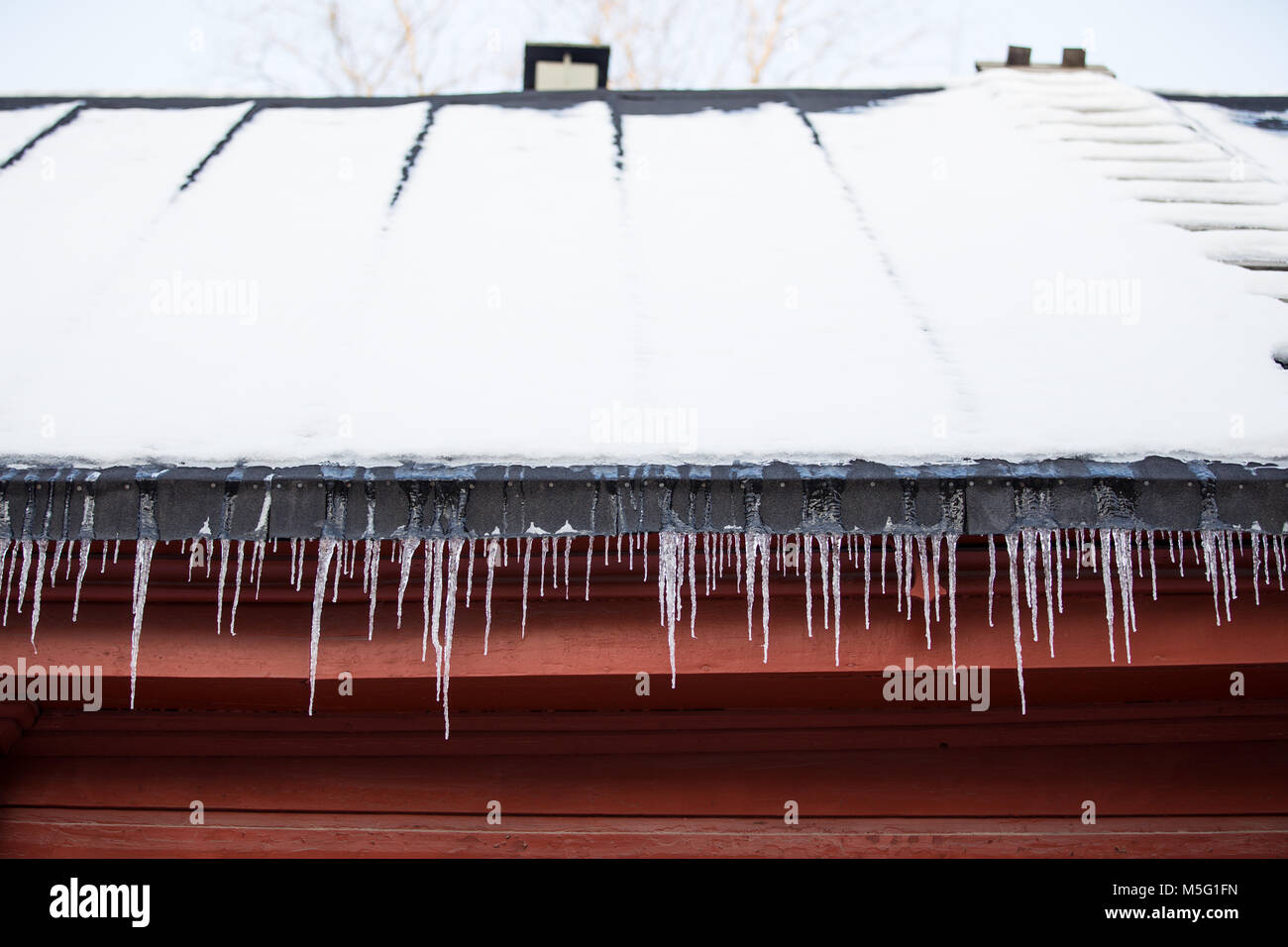 Detail of icicles hanging from snow covered roof on red wooden building Stock Photo