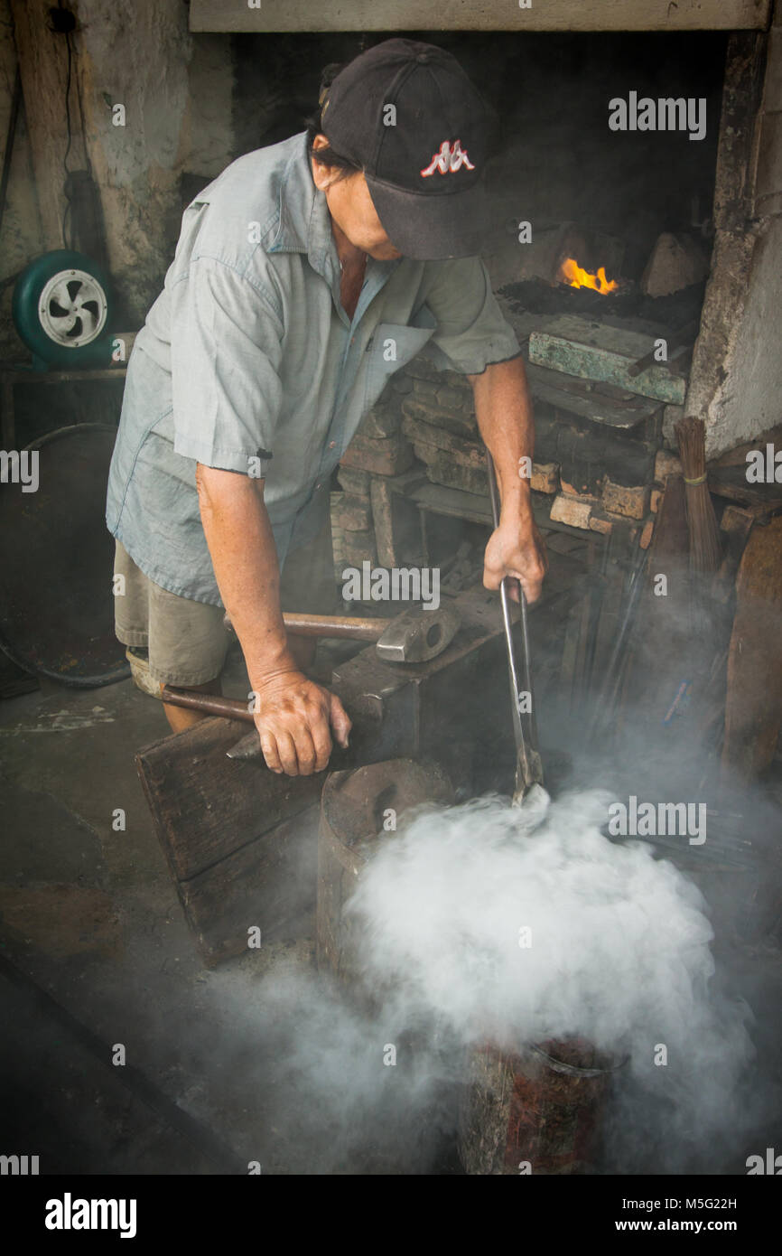 Malaysian Blacksmith cooling red hot iron work tools after being heat treated and shaped. Steam rises dramatically from the water as he dips the iron Stock Photo