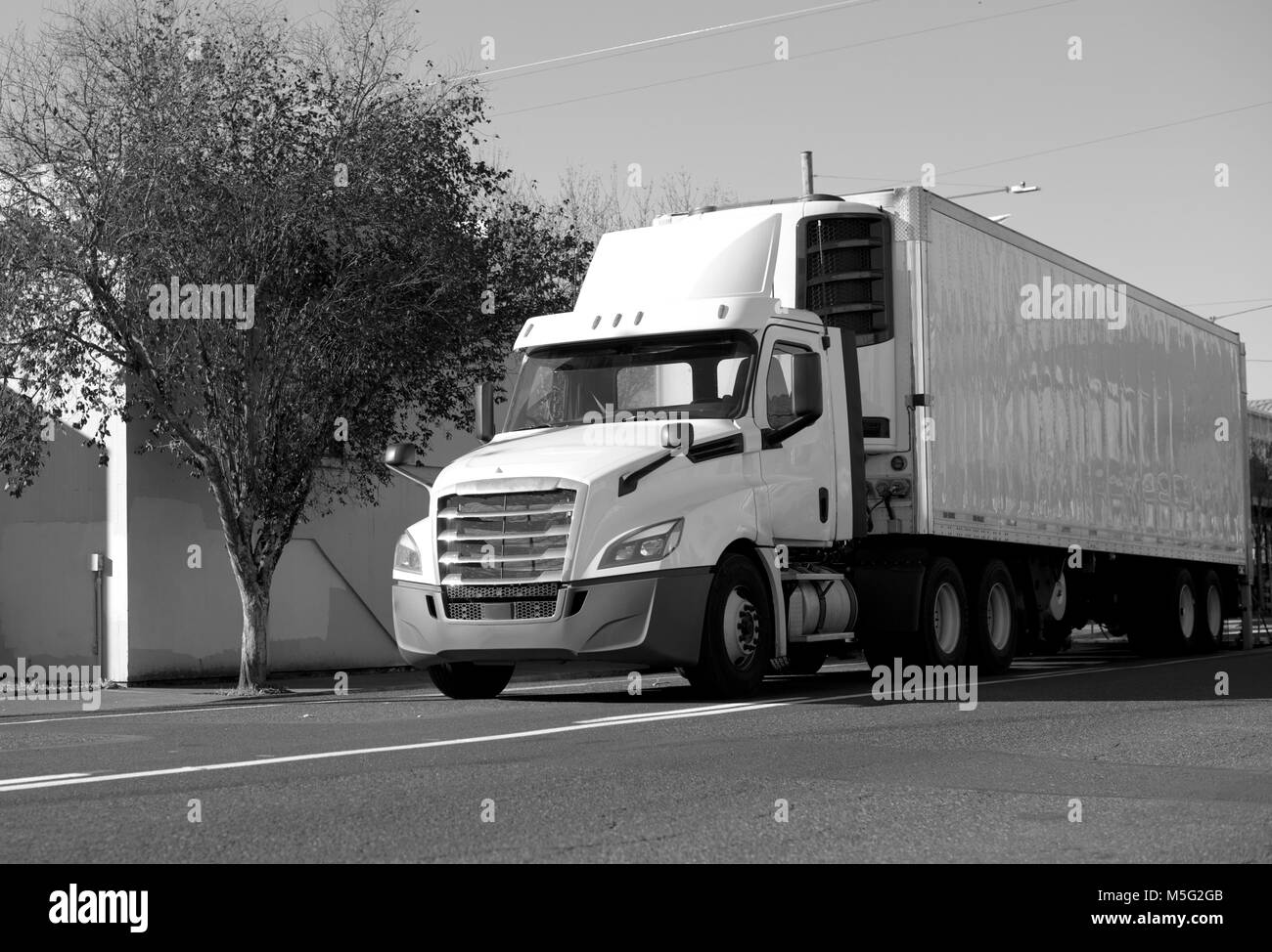 Modern day cab big rig semi truck for short local deliveries with refrigerator semi trailer for transporting frozen food running on the city street Stock Photo